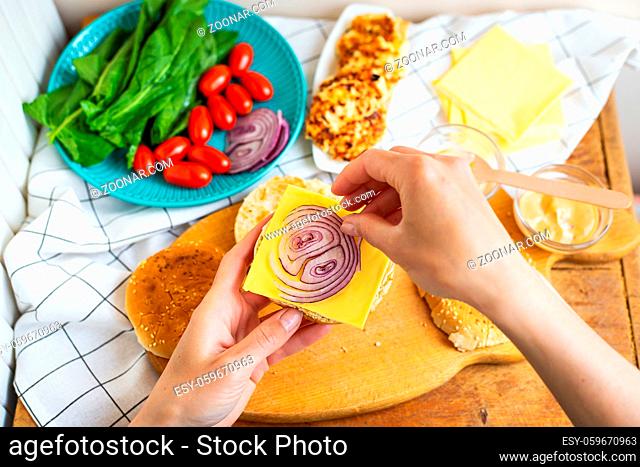 Preparation of all the ingredients for making a burger - bun, cutlet, cheese, salad, tomato, sauces. Top view, girl's hands take a burger bun and lay on a...