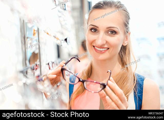 Beautiful woman in optician store chooses her glasses looking pleased