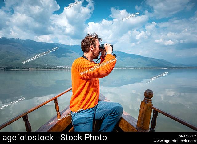 Man birdwatching on a boat, the lake is surrounded by mountains