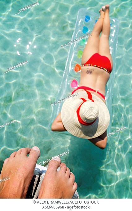 Woman floating on lilo in tropical lagoon with man above watching