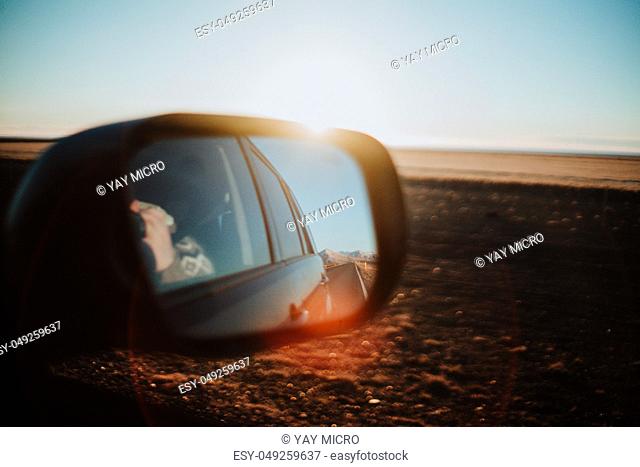The view through the back mirror of a car onto an Icelandic landscape at sunset
