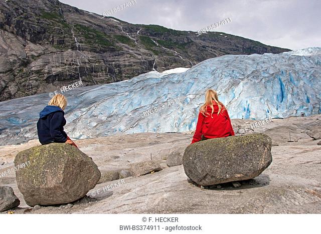 two children sitting on rocks in front of Nigardsbreen glacier, Norway, Jostedalsbreen National Park