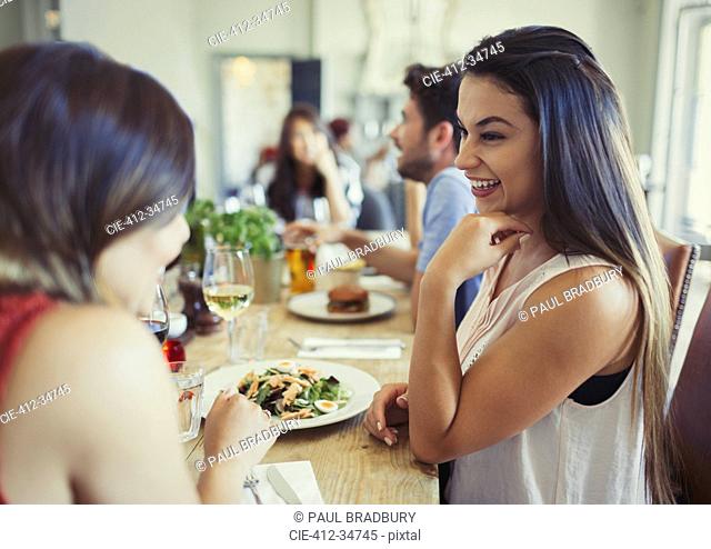 Smiling women friends talking and eating at restaurant table