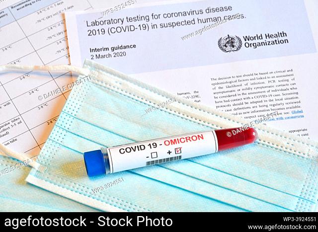 Florence: New Omicron variant of the Covid 19 Virus. Test tube with positive Omicron COVID-19 test blood sample on protective medical masks and documents