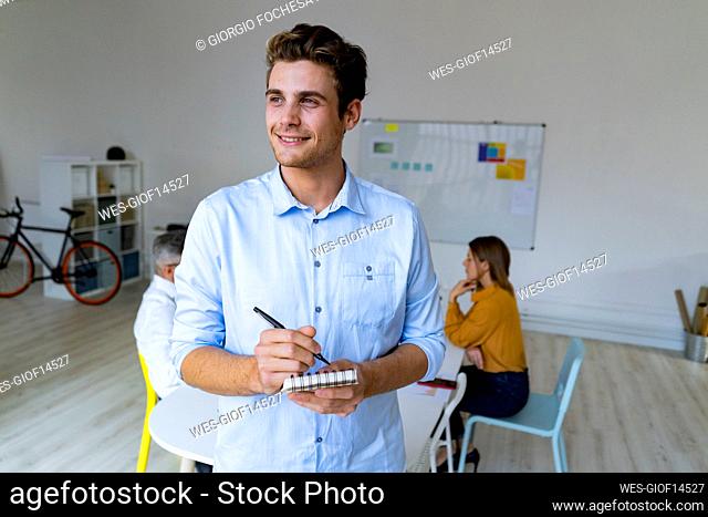 Contemplative businessman with notepad and pen standing in office