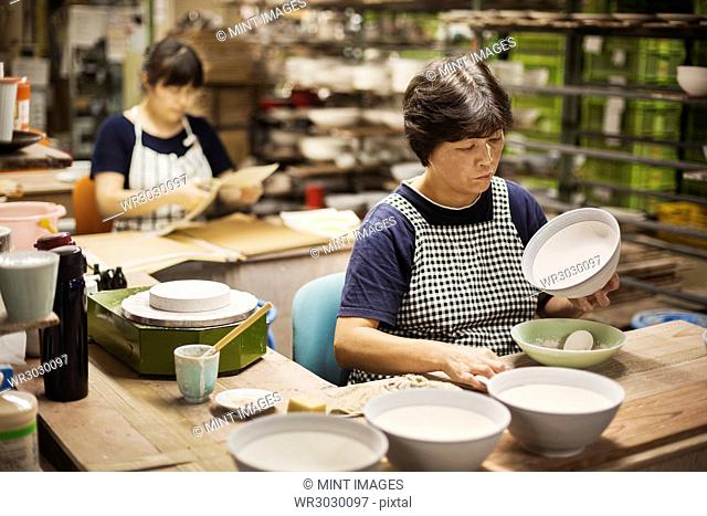 Two women sitting in a workshop, working on Japanese porcelain bowls