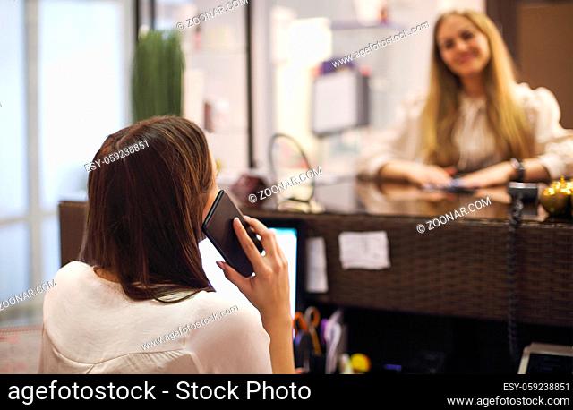 Young female receptionist working in beauty salon and writing down appointment of anonymous female customer