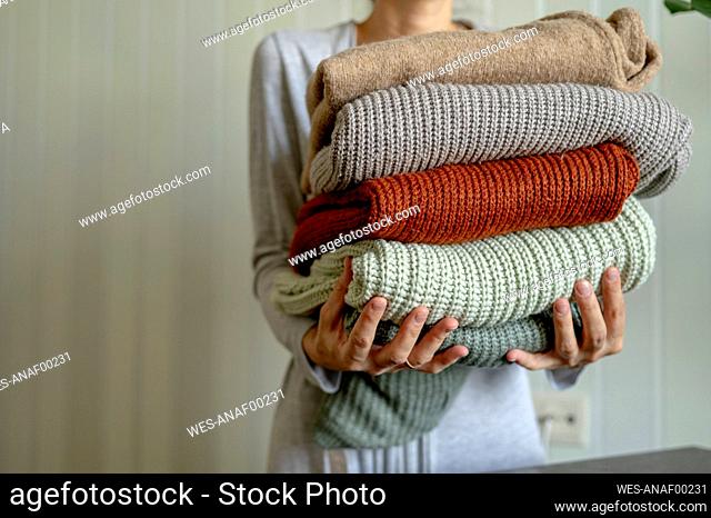 Woman holding multi colored sweaters at home