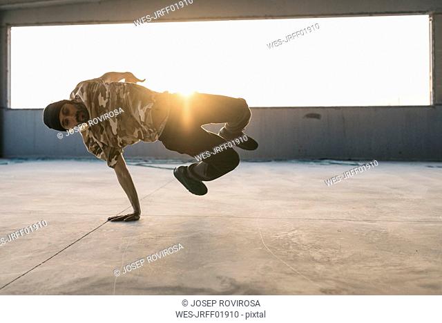 Man doing breakdance in urban concrete building, standing on hand