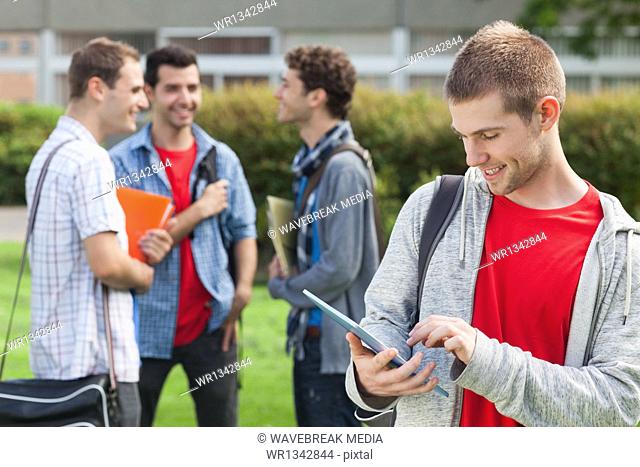 Cheerful male student using his tablet in front of his classmates outside