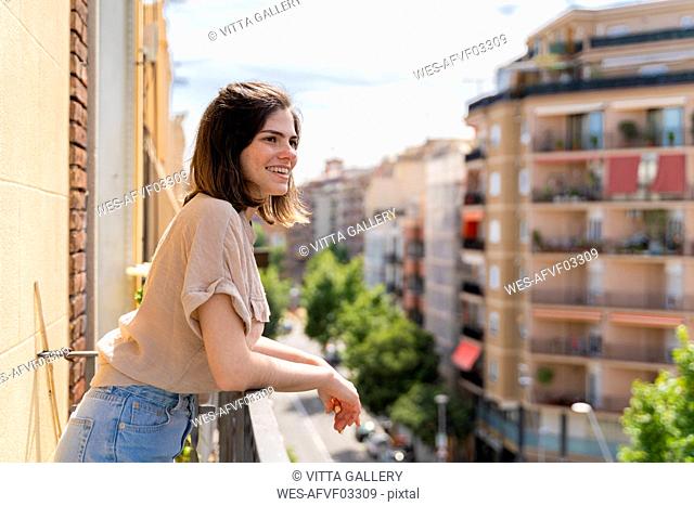 Happy young woman standing on balcony in the city