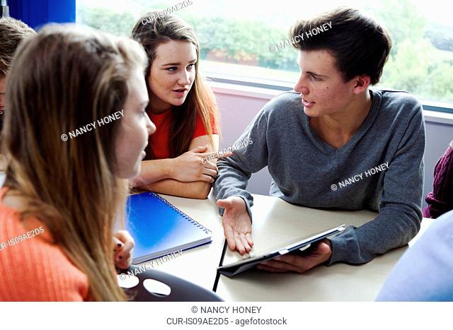 Teenage schoolchildren sitting at desk using digital tablet