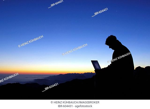 Man with laptop at sunrise on a mountain top, Breitenstein Mountain, Bavarian foothills, Wendelstein Group, Upper Bavaria, Bavaria, Germany