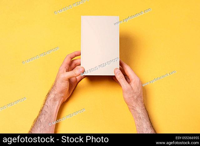Male hands holding a small box in front of yellow background, mock-up series template ready for your design, face selection path included