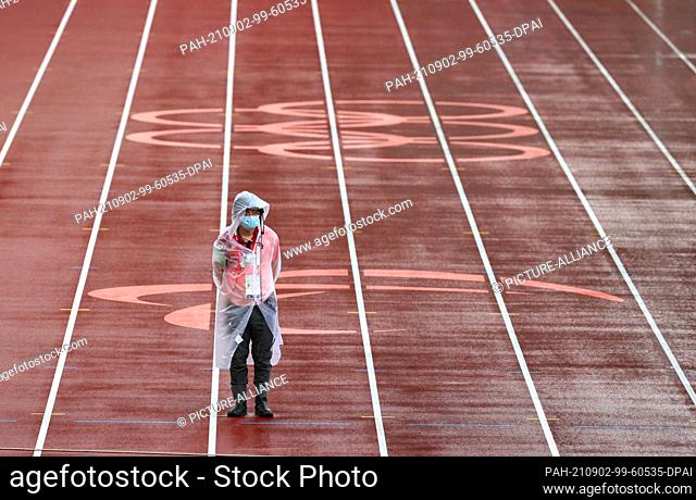 02 September 2021, Japan, Tokio: Paralympics: Athletics, at the Olympic Stadium. A helper stands on the tartan track in the rain