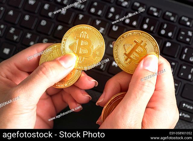 Woman hand holding golden coloured bitcoin coins over black laptop keyboard