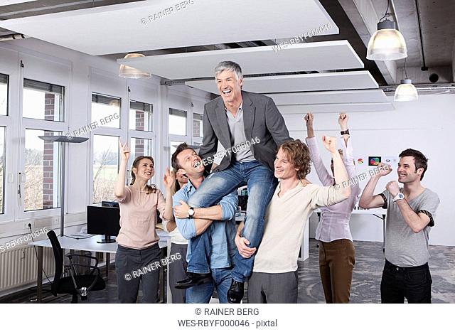 Germany, Bavaria, Munich, Colleagues carrying mature man on shoulder, smiling