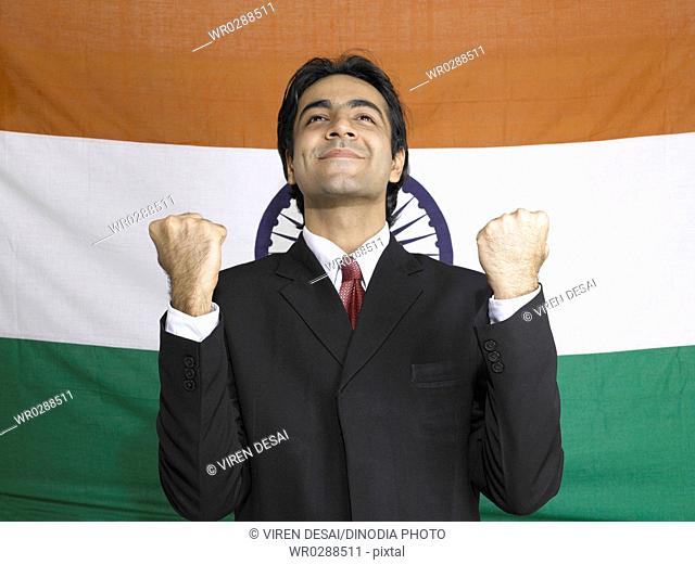 South Asian Indian executive looking above raising fists standing in front of flag of India in background MR702A