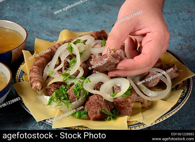 Beshbarmak - National Kazakh dish, prepared with meat and pasta. Beshbarmak dish close-up on a plate on the table. Large pieces of stewed meat and onion