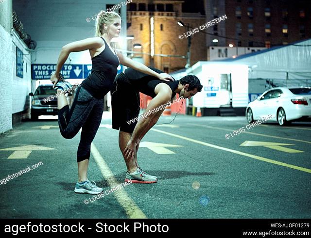 Couple doing stretching exercise during night on road in city