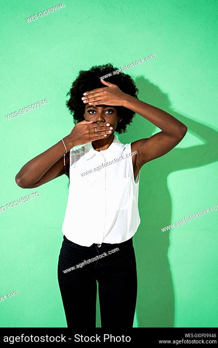 Woman covering face with hands while standing against green background