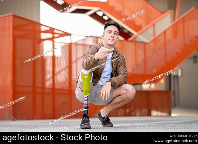 Young disabled man crouching while showing obscene gesture against staircase