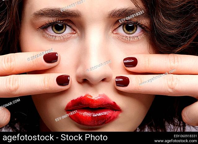 Closeup beauty portrait of young woman with hands near face. Brunette girl with unusual alyapy red female face makeup