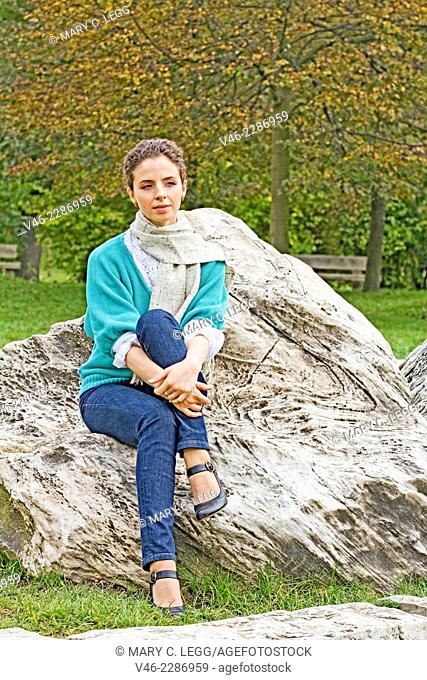 Woman in aqua sweater and blue jeans seated on a rock