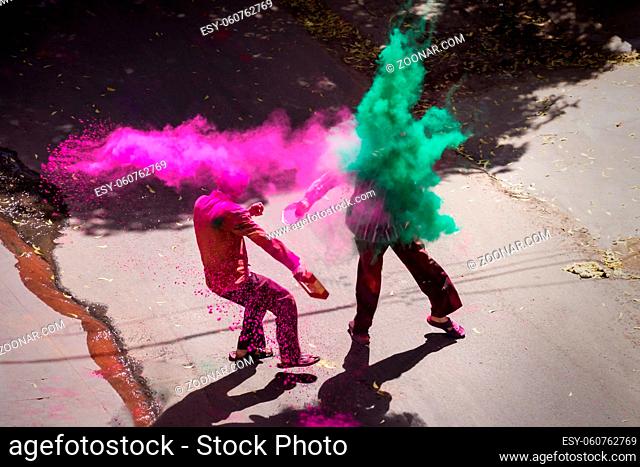 Two indian men throwing paint in colorful powder clouds for Holi, Jaipur, Rajasthan, India