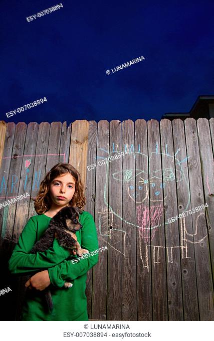 children girl holding puppy dog after chalk painting on backyard wood fence