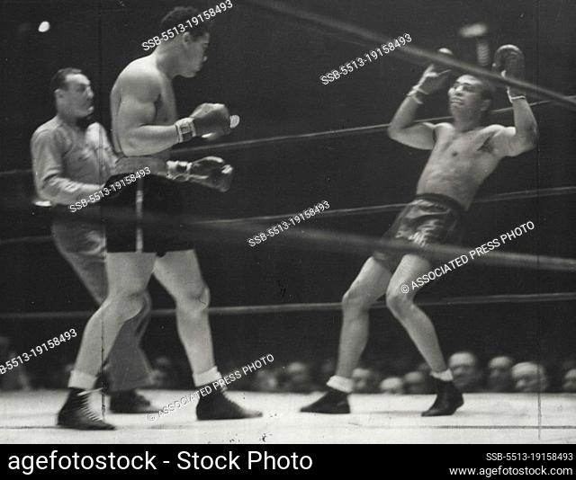 Lewis Surrenders -- Dazed and reeling under a barrage by Champion Joe Louis, John Henry Lewis the challenger is shown as he tossed his hands in the air in an...