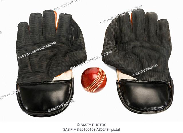 Close-up of a cricket ball with a pair of wicket keeping gloves