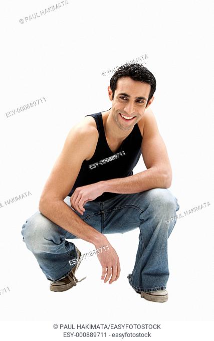 Handsome smiling Caucasian guy wearing black tank top and jeans squatting, isolated