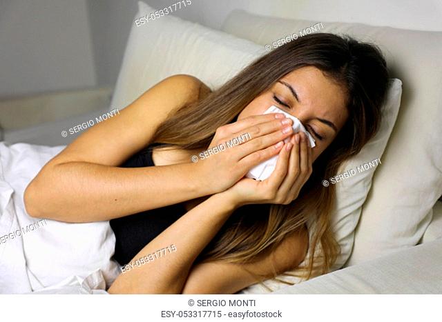 Young sick girl with fever clean nose after sneezing in the bed at night
