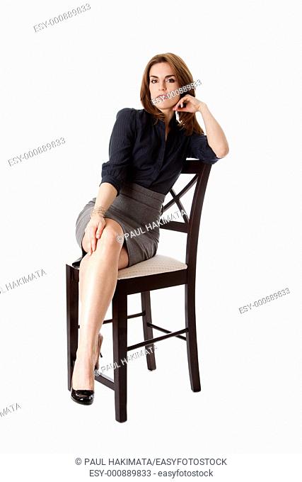 Beautiful brunette business woman sitting wearing gray skirt and blue blouse with hand on leg with legs crossed, isolated