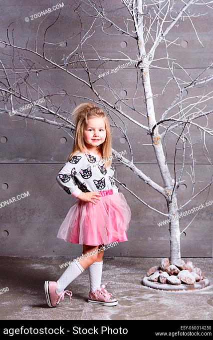 Pretty girl child 3 years old in a pink dress. in holiday gray room with tree