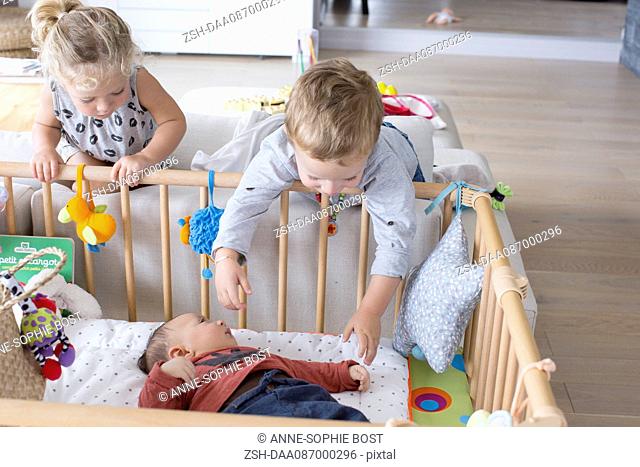 Children leaning over the side of baby brother's crib