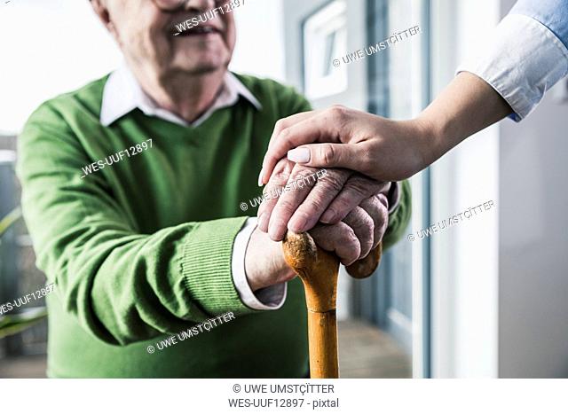 Close-up of woman holding senior man's hand leaning on cane