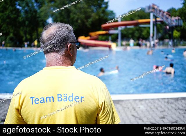 17 June 2022, Baden-Wuerttemberg, Mannheim: A lifeguard stands in front of a pool with a water slide at Herzogenriedbad. Because of the lack of lifeguards