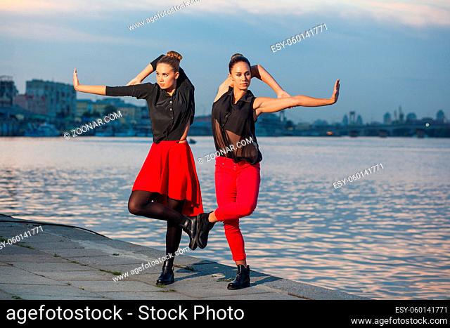 Two young beautiful twin sisters are dancing waacking dance in the city background near river. showing the different style and pose of modern dance with black...