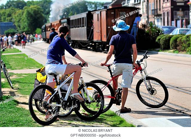 A COUPLE OF CYCLISTS LOOKING AT THE LITTLE SIGHTSEEING STEAM LOCOMOTIVE OF THE BAY OF SOMME, TRAIN STATION IN SAINT-VALERY-SUR-SOMME, SOMME 80, FRANCE