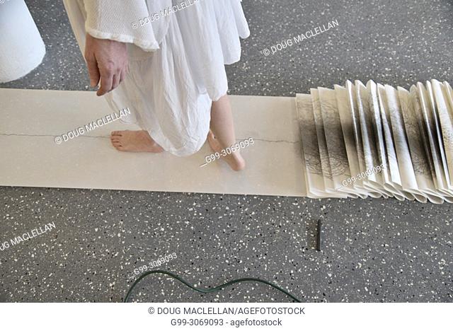 A side view from the knees down of a woman artist in a white dress turning as she creates a performance art work at an artist run gallery in Windsor, Canada
