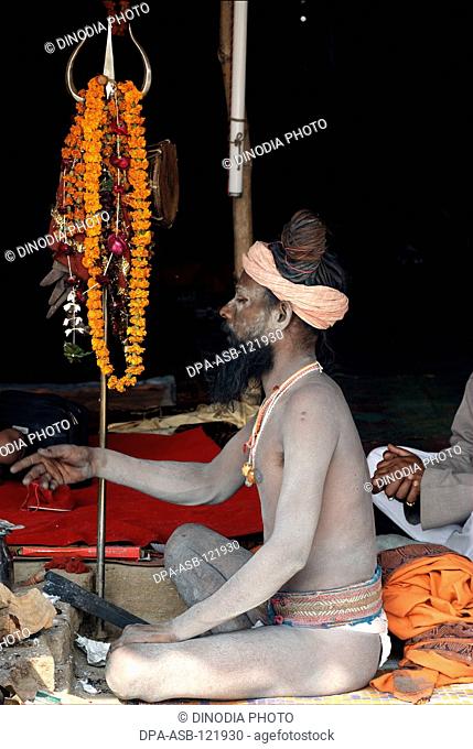 A naga sadhu from the Juna Akadha sits with his Trishul at their camp during the Ardh Kumbh Mela , , , India