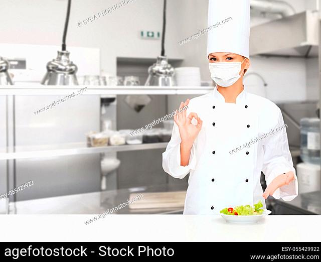 female chef in mask showing ok sign at kitchen