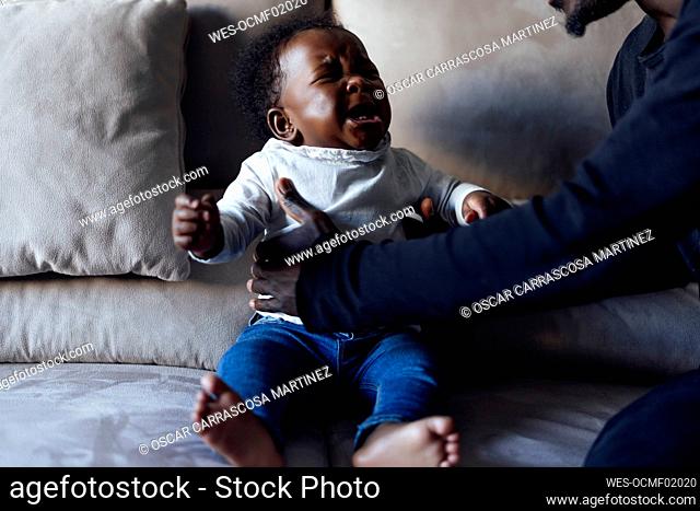 Father lifting crying baby daughter on sofa in living room