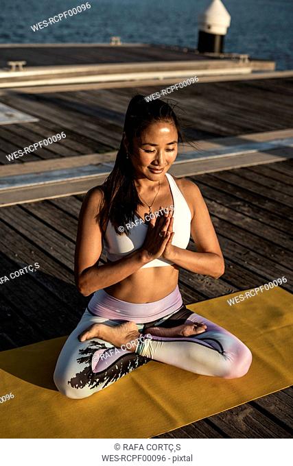 Asian woman practicing yoga on a pier at harbour