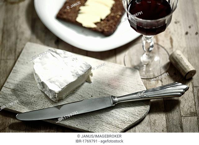 Dining table with whole grain bread, soft cheese, red wine and cutlery