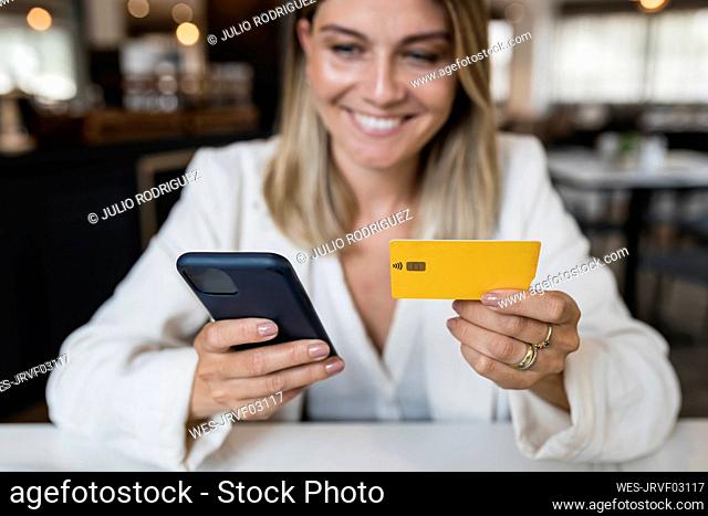 Smiling businesswoman holding credit card doing online shopping through smart phone at restaurant