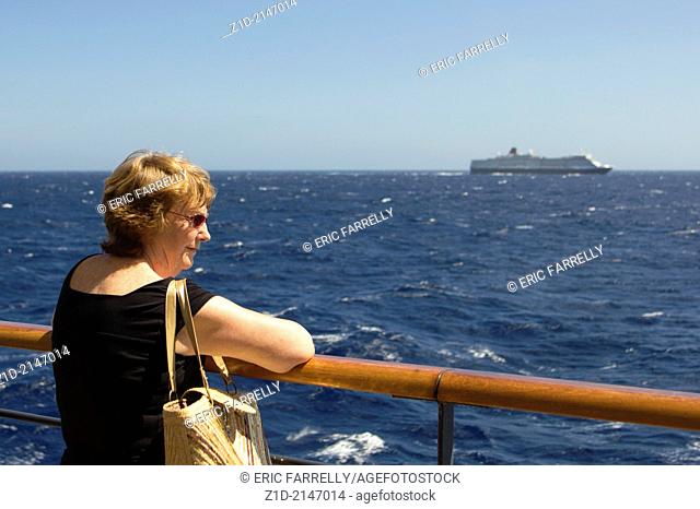 older woman enjoying seaview from the rails of the cunard liner ""Queen Victoria"", with Cunard liner Queen Elizabeth sailing in parallel with sister ship