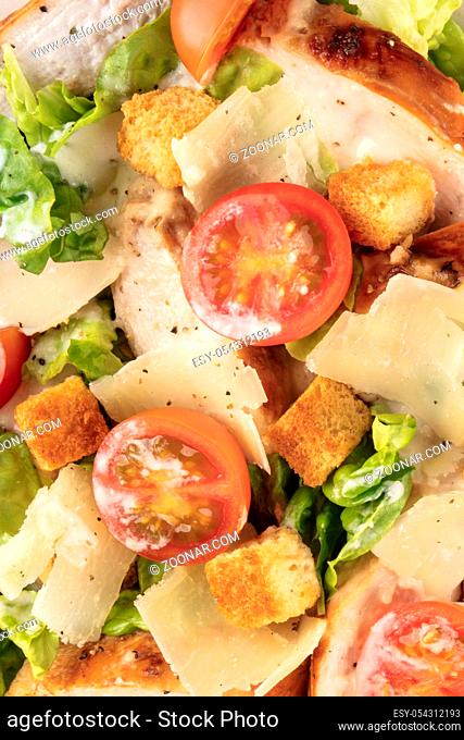 Caesar salad texture. Slices of chicken breast, green lettuce, Parmesan cheese, croutons, and cherry tomatoes, shot from the top with the typical dressing